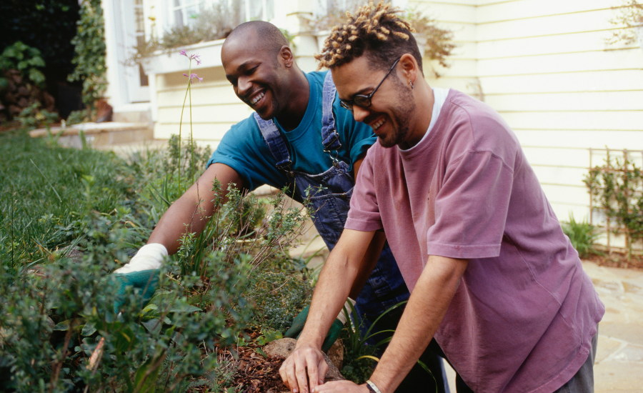 Two People of Color are standing together and laughing while gardening together.