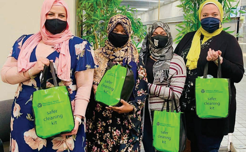 Four Mother Africa staff are standing together holding green reusable bags and wearing face masks to prevent the spread of viral infections.