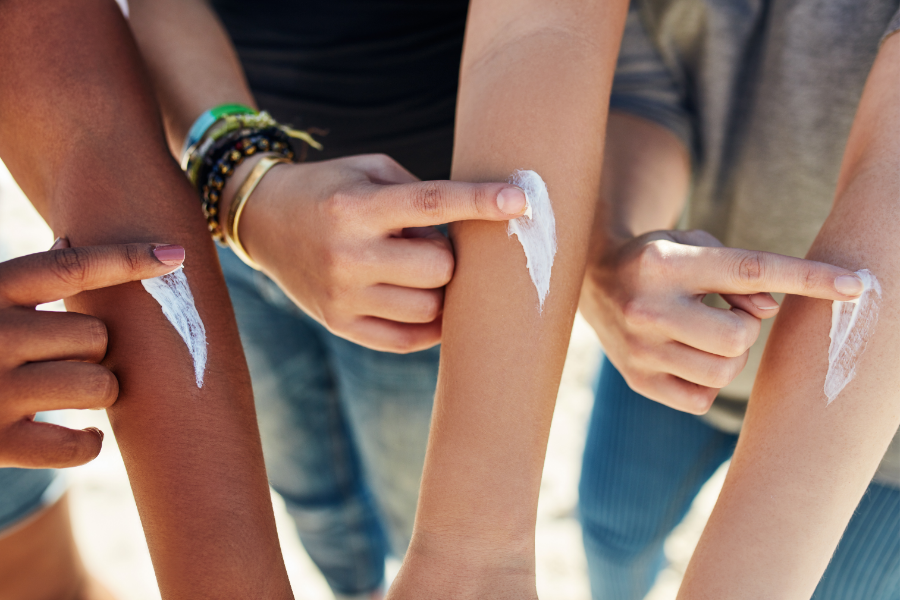 Three people rubbing sunscreen on their arms